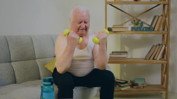 Domu Salonie Dobrze Wyglądający Staruszek Siedzi Kanapie Podnosi Ciężary Trenując — Wideo stockowe