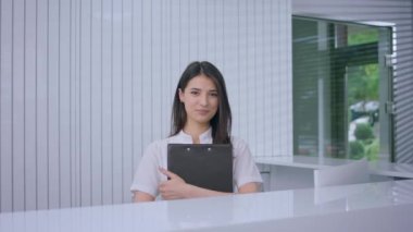 Resepsiyondaki kameraya poz veren güzel tıbbi asistanın önünde elinde belgelerle elinde bir harita tutarak gülümsüyor..