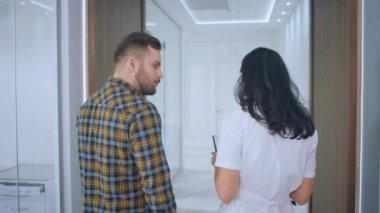 Modern ve ferah klinik hastası bir adam hemşirelerle birlikte yürüyor ve koridorda yürürken kan testinin sonuçlarını tartışıyor..