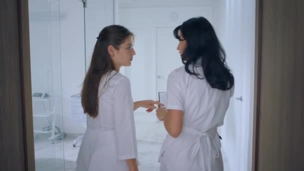 大規模な白い診療所では 2人の看護師が診療所を歩き 白い制服を着て何かを話し合います — ストック動画
