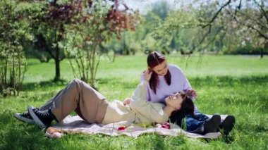 Güzel iki bayan lezbiyen parkın ortasında çimlere uzanıp birbirlerine sarılıyorlar ve aşkla besleniyorlar. 4k