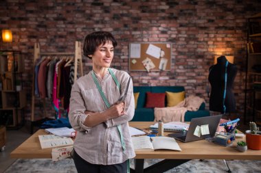 Modern terzisindeki karizmatik ve çekici terzi kadının önünde poz vererek terzi makasını tutuyor ve tatlı tatlı gülümsüyor..