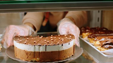 Fırın kafeteryasında kameraya yakın çekim yapan bir satıcının videosu var. Vitrindeki çikolatalı pastayı dikkatlice düzenle..