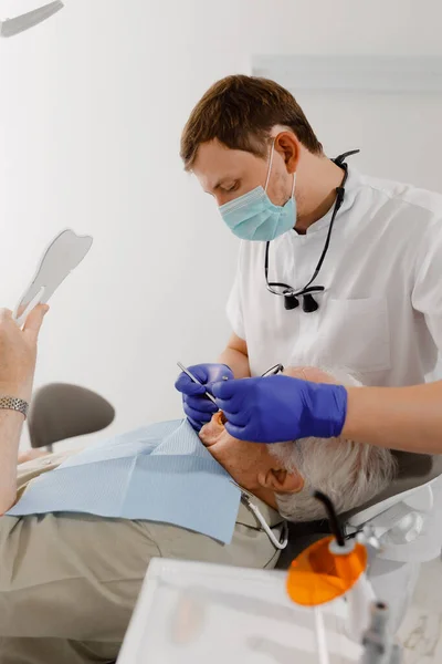 老人のための口腔ケア治療は 彼が歯医者の椅子に横たわっていた歯科医を訪問し 治療のための医療機器を使用して医師を検査するために来ました 歯医者 — ストック写真
