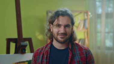 Çok yakışıklı bir ressam ressamın önünde duruyor ve kameraya gülümsüyor.