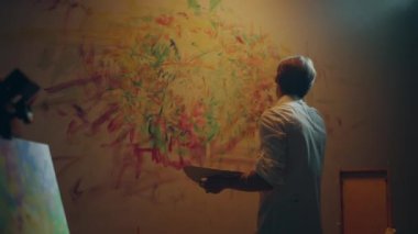 Sanat stüdyosundaki genç ve yetenekli sanatçı parmaklarıyla duvar resmi çiziyor. Renk paletini elinde tutuyor. 4k