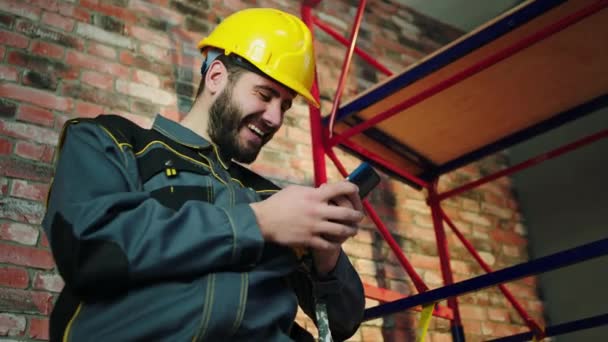 建筑工地富有魅力的工头高兴而兴奋地使用智能手机观看他戴着安全帽和装备的东西 — 图库视频影像