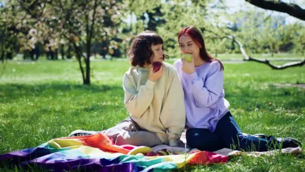 公園の中でレズビアンの女性は一緒にピクニックをしている彼らは一緒にいくつかの果物を食べて 大きな笑顔は一緒に時間をお楽しみください — ストック動画