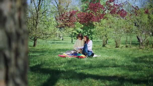 ライトカップルは非常にカリスマ的なピクニック時間を持っています自然の中で彼らはデジタルタブレットを見て 一緒に太陽を楽しんでいます — ストック動画
