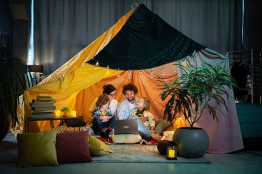 Çocuk odasındaki el yapımı çadırda otururken aile babaları ve onların iki küçük çocuğuyla birlikte dizüstü bilgisayarda film izleyerek iyi vakit geçir. Aile