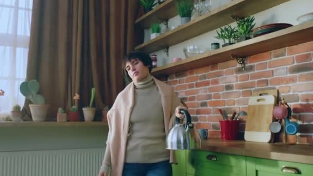 在家里的厨房里 漂亮的短发女人看起来很疲倦 她拿着水壶放在电炉上做了一杯热饮 — 图库视频影像