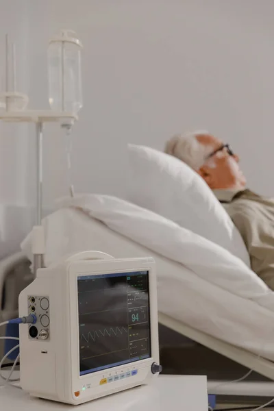 在医院的沙发上 老人躺在床上 一边吃着检查 一边戴着心率监测器 — 图库照片