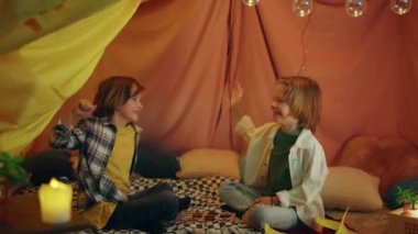 Two really young cute and charming boys are having fun and high fiving eachother in a big comfy indoor tent.