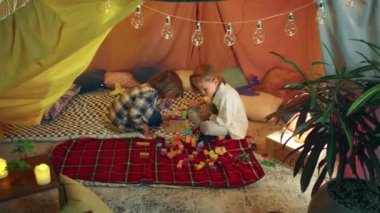 İki neşeli genç, kapalı bir çadırda ahşap renkli bloklarla birlikte oynuyorlar..
