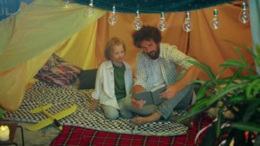 Aile zamanı kavramı yakışıklı baba ve oğlu çocuk odasında çadırın içinde otururken birlikte bir kitap hazırlıyorlar..