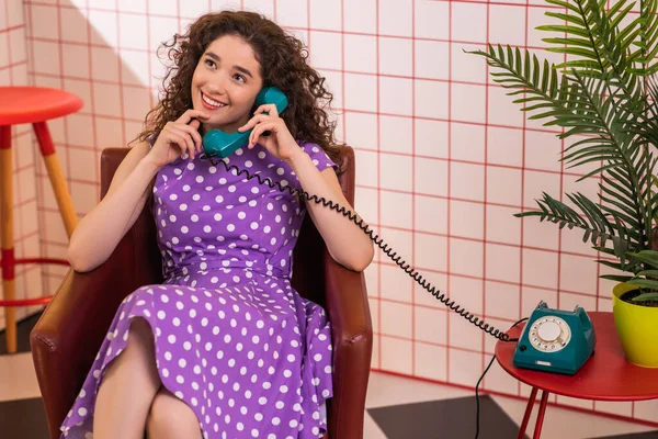 stock image Attractive woman with a perfect smile take the landline phone and start to discussing while she is sitting on the sofa in the kitchen. Retro
