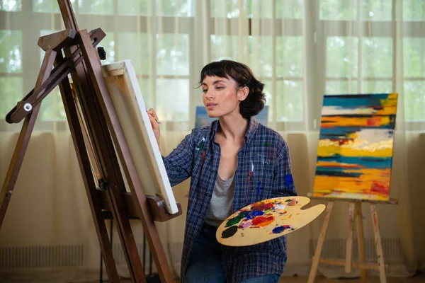 油絵具で魅力的な女の子の絵画 白い背景の上に仕事でプロの画家 若い女性アーティストのスタジオポートレート — ストック写真
