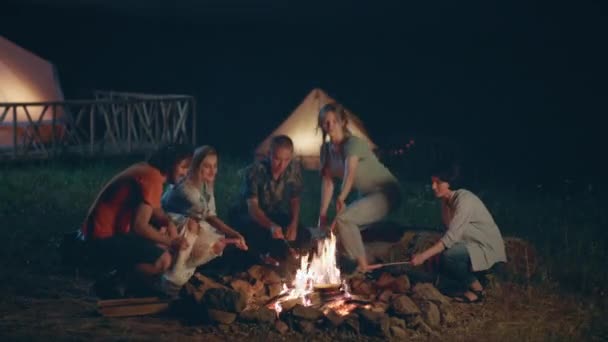 キャンプ場で友人のグループのための自然の中で楽しい時間は 火の杭でいくつかのソーセージを調理し 一緒に夕食を準備します — ストック動画