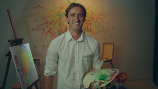 在艺术演播室里 有魅力的艺术家在镜头前摆姿势 面带微笑 手里拿着油彩调色板 — 图库视频影像