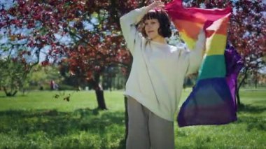 Parkta karizmatik Igbt kadını gökkuşağı lgbt bayrağını alır ve sırtına koyar ve kameraya poz verir. 4