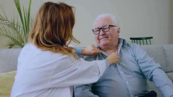 リビングルームで老人はソファーに座り 聴診器を使ったグランプリで患者さんの健康診断を待っている — ストック動画
