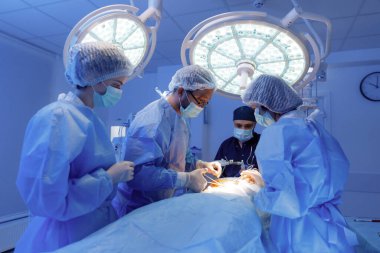 Four people in a surgical room are discussing and performing a stomach surgery on a patient.