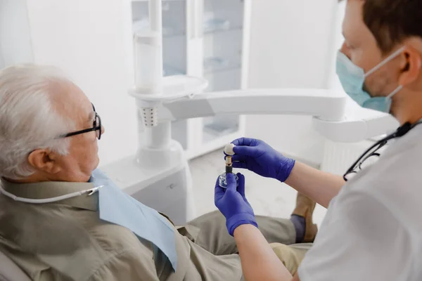 老人患者は歯医者に歯医者の診察を予約します彼は提出の問題をチェックする歯科機器を使用して歯医者を調べます — ストック写真
