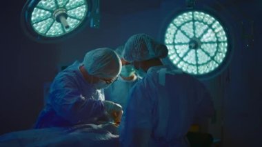 Two nurses and a surgeon all wearing scrubs and surgical gear are operating on a patient and the nurses are watching very intensely as the surgeon is performing the surgery. Shot on ARRI