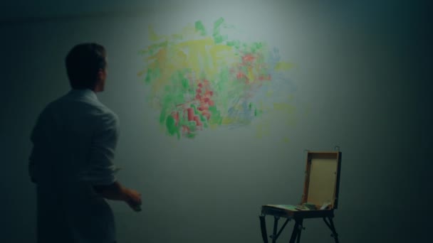 一个英俊的艺术家在他的艺术工作室的墙上画了一幅现代绘画 他用的是油彩和画笔 — 图库视频影像