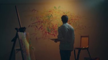 Modern sanat ressamı, resim stüdyosunun duvarına yağlı boya boya ve parmaklar kullanarak resim yapıyor. 4k