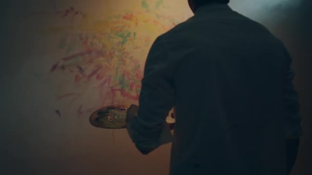 艺术家手里拿着他的油彩调色板 用手指在他的艺术工作室的墙上画这幅画 — 图库视频影像