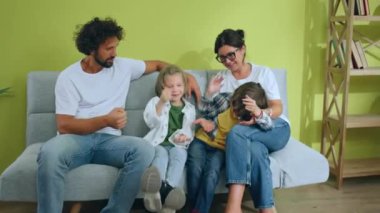 In front of the camera happy two kids and their parents moving in the new home they enjoy the time together playing Rock Paper Scissors while sitting down on the new sofa. 4k