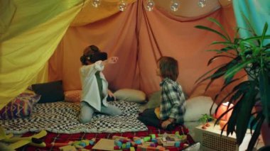 Two boys are hanging out in a children s blanket tent indoors while playing with a vr headset and enjoying their time laughing together. 4k