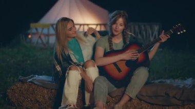 Kamp alanındaki iki iyi arkadaş ateş kazığının yanında oturmuş birbirlerine sarılarak gitar çalan bir bayan görüyorlar. ARRI 'de çekilen