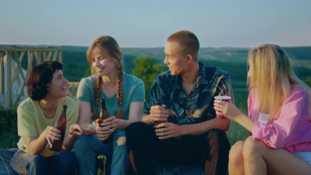 3人の女の子と1人の男が 山や自然に囲まれた外に座り 飲み物を分かち合い 笑いながらお互いの会社を楽しんでいる 4Kについて — ストック動画