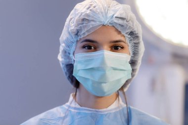 A very close up shot of a beautiful nurse with brown eyes and eyebrows wearing a medical mask and hairnet straying directly at the camera.