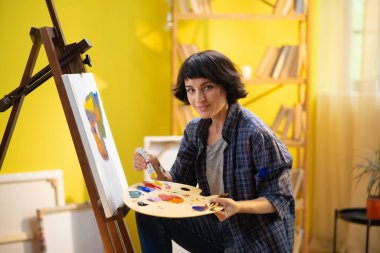 Bir kadının fırçasını iş paletine batırdığı ve çok konsantre olduğu bir sırada bir portreye resim yaptığı yakın plan bir fotoğraf. ressam