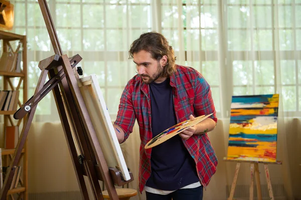 stock image A closing up shot of a very handsome painter man working on a new modern painting while sitting down in a chair and admiring his work in front of him. Paint