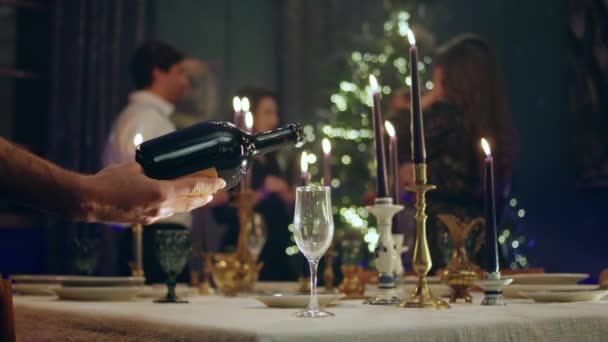 クリスマスディナーテーブルにスパークリングワインのビデオグラスをキャプチャするカメラの前に 誰かがクリスマスを祝う人々の背景グループのグラスに輝くものを注ぐ — ストック動画