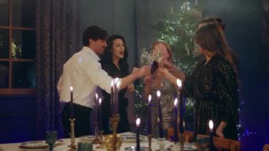 Yılbaşı gecesi arkadaş grubu çok karizmatik ve mutlu bir şekilde Noel ağacının yanında kutluyorlar ve yemek masası şampanya kadehleriyle tezahürat yapıyor. 4k
