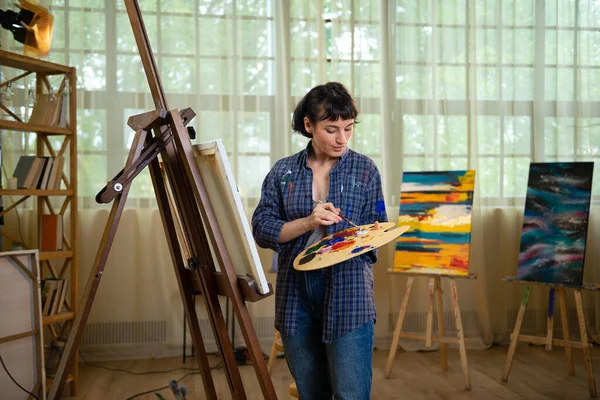 油絵具で魅力的な女の子の絵画 白い背景の上に仕事でプロの画家 若い女性アーティストのスタジオポートレート — ストック写真