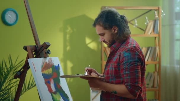 一个有着中等头发和胡子的英俊画家盯着他的艺术作品 用他的刷子和调色板在上面画画 向Arri Alexa开枪 — 图库视频影像