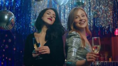 Gece kulübünde, kameranın önünde gülümseyen karizmatik, muhteşem elbiseli iki kadın yeni yılı ya da Noel 'i kutluyorlar. 4k