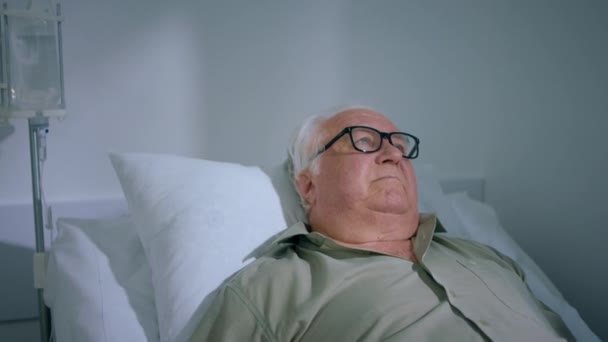 病院のソファに横たわる老人の患者 彼は指の心拍数モニターのパルス パルスの近似値を測定しています — ストック動画
