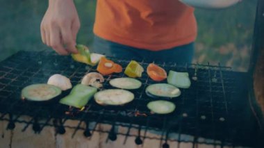 Turuncu bluz giyen, bir sürü sebzeyi eski ızgaraya koyup buharlaştıran ve pişiren bir adamın yakın plan fotoğrafı. 4k