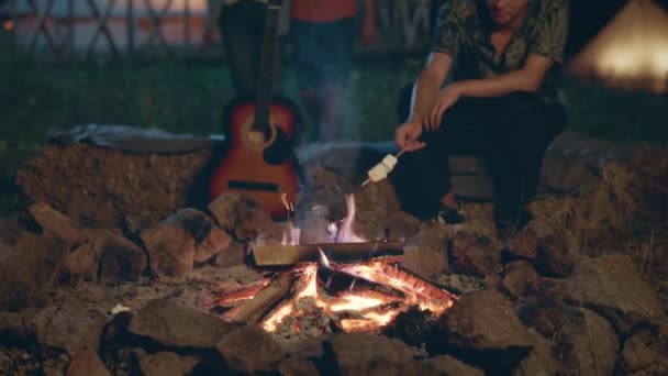 良い友人のキャンプ場グループでは 非常にカリスマ性が火災のステークの横に座って 良い時間を過ごすと いくつかのマシュマロを調理するギターを取ります Arriで撮影する — ストック動画