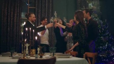 Yeni yılı birlikte kutlayan bir grup yakışıklı arkadaş muhteşem Noel ağacının yanında durup oturma odasındaki yemek masasının üzerinde şampanya bardaklarıyla tezahürat yapıyorlar. 4k