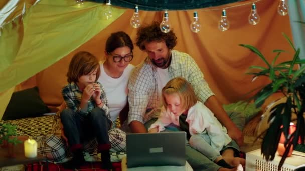 テントの中に座っている間 子供部屋の両親と2人の小さな男の子の大きな延長テントで一緒にラップトップで映画を見ています 4Kについて — ストック動画