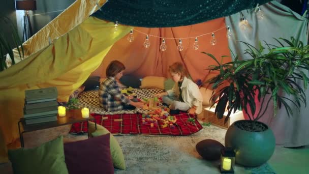 两个小男孩正在一个五颜六色的毛毯堡垒里玩彩虹色的积木 — 图库视频影像