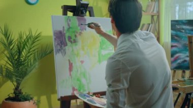 Sanat stüdyosunda karizmatik bir sanatçı tuvale resim yapıyor. Yeni bir resim. Paletin yağlı rengini tutkuyla kullanıyor..